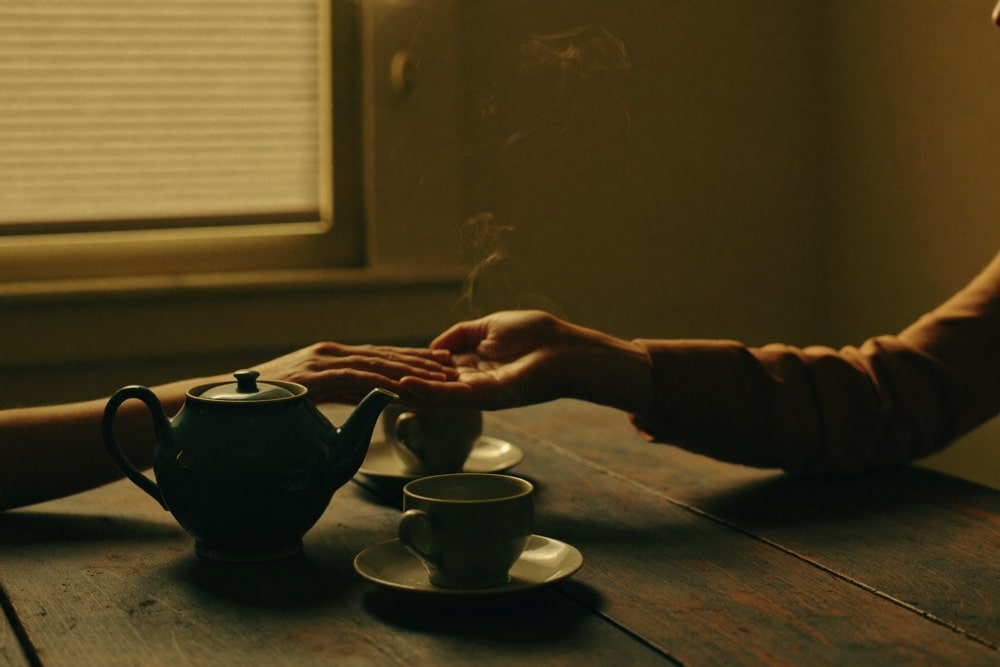 Two people's hands meeting across a kitchen table beside a teapot