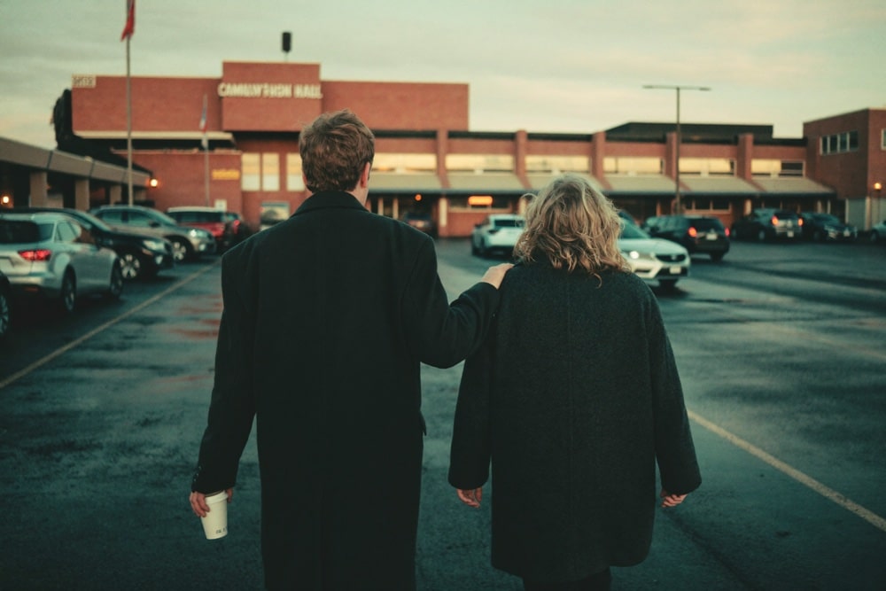 Two people walking together across a car park towards a community hall at dusk